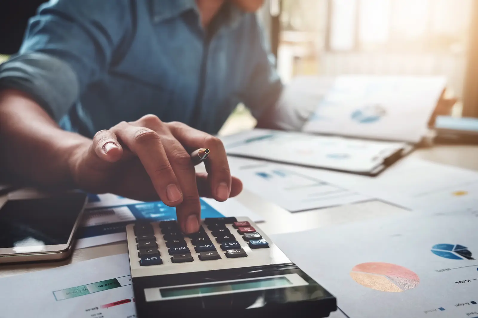 Mains d'un comptable vérifiant une convention de subvention avec une calculatrice sur le bureau
